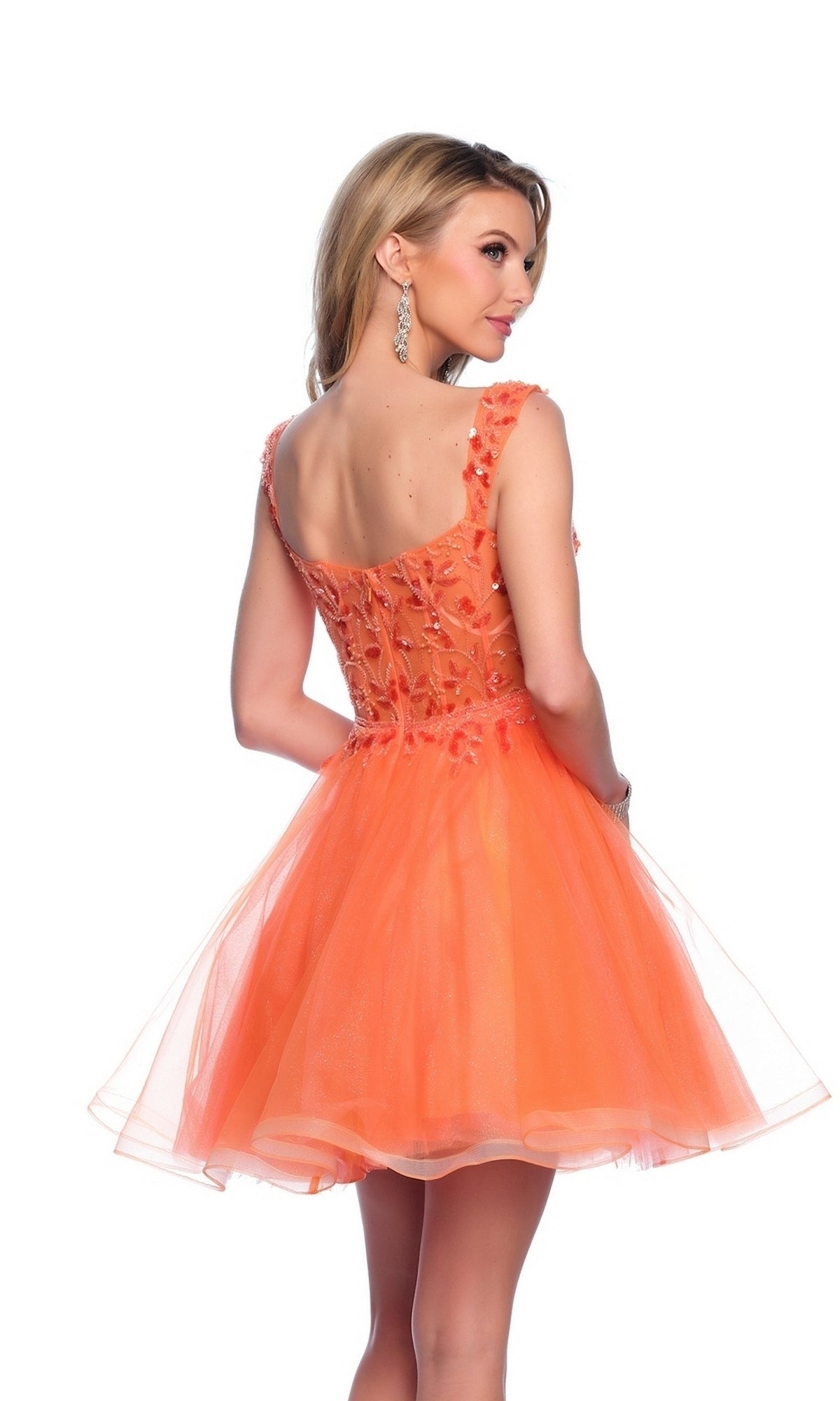 A woman in the Orange Homecoming Dress 12038, a sleeveless knee-length dress with floral embellishments, stands facing away and looks over her shoulder.